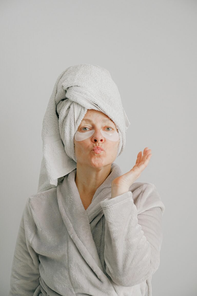 Woman with a towel on her head and eye masks, blowing a kiss in a robe.