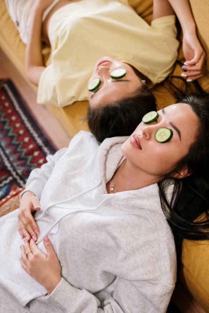 Two women enjoying a spa day at home with cucumber masks for skincare relaxation.