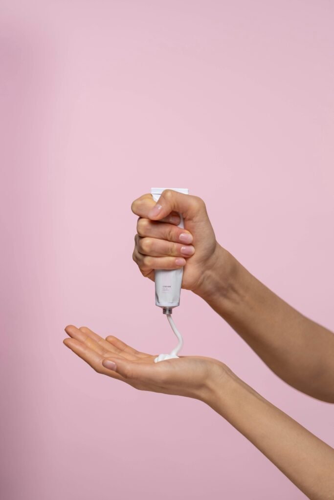 Close-up of a person applying cream from a tube against a pink backdrop.